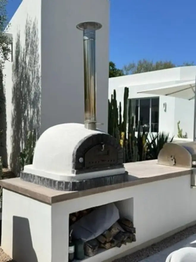 Stainless chimney cap topping a tall extension on a stucco brick pizza oven with a wood store below