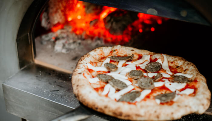Pizza cooking in a wood fired outdoor pizza oven with mushroom and vegetable toppings on a cordierite stone