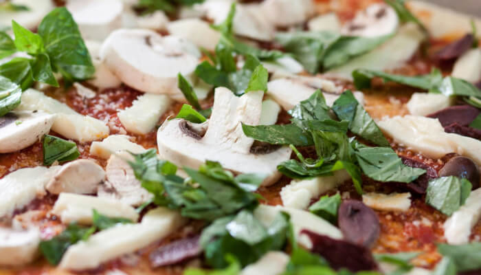 Fresh mushroom pizza with basil spinach and vegetables on crispy crust cooked in outdoor pizza oven
