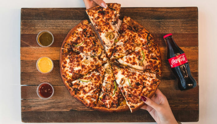 Sliced chicken pizza on a wooden board with dipping sauces and a Coca-Cola bottle, showing the finished result of a homemade chicken pizza crust recipe