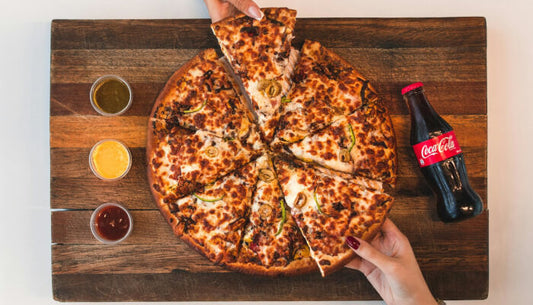 Sliced chicken pizza on a wooden board with dipping sauces and a Coca-Cola bottle, showing the finished result of a homemade chicken pizza crust recipe