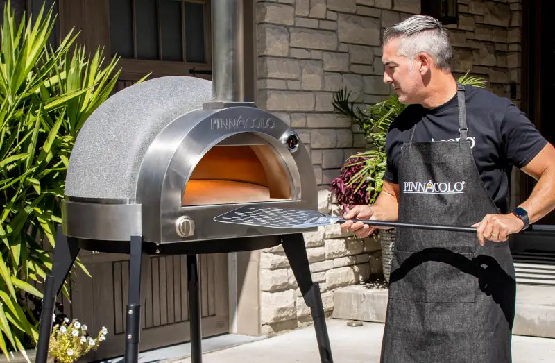 Man loading a pizza into a premium outdoor pizza oven on a backyard patio, showing whether an outdoor pizza oven is worth it