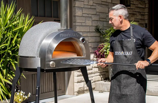 Man loading a pizza into a premium outdoor pizza oven on a backyard patio, showing whether an outdoor pizza oven is worth it