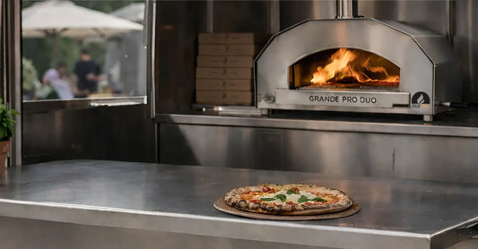 ItaliaForno Grande Pro Duo hybrid pizza oven on a stainless counter inside a pizza trailer with the serving window open