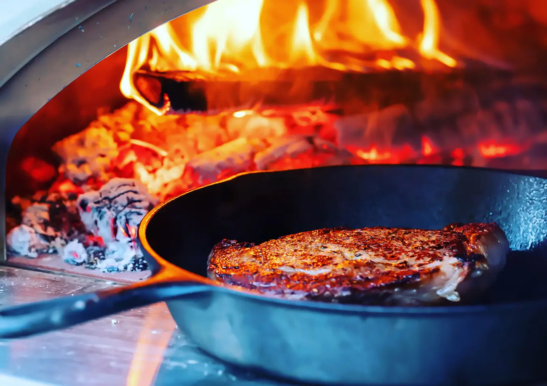 Seared ribeye steak in a cast iron skillet inside a wood-fired pizza oven