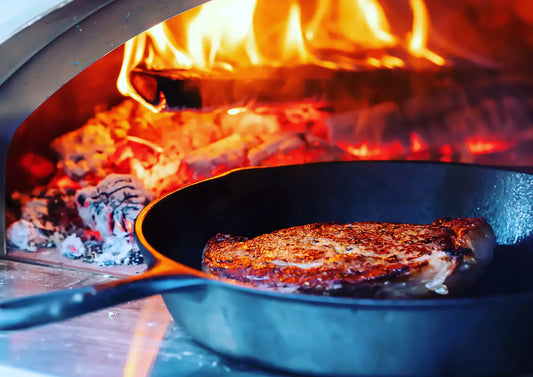 Seared ribeye steak in a cast iron skillet inside a wood-fired pizza oven