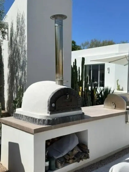 Stainless chimney cap topping a tall extension on a stucco brick pizza oven with a wood store below