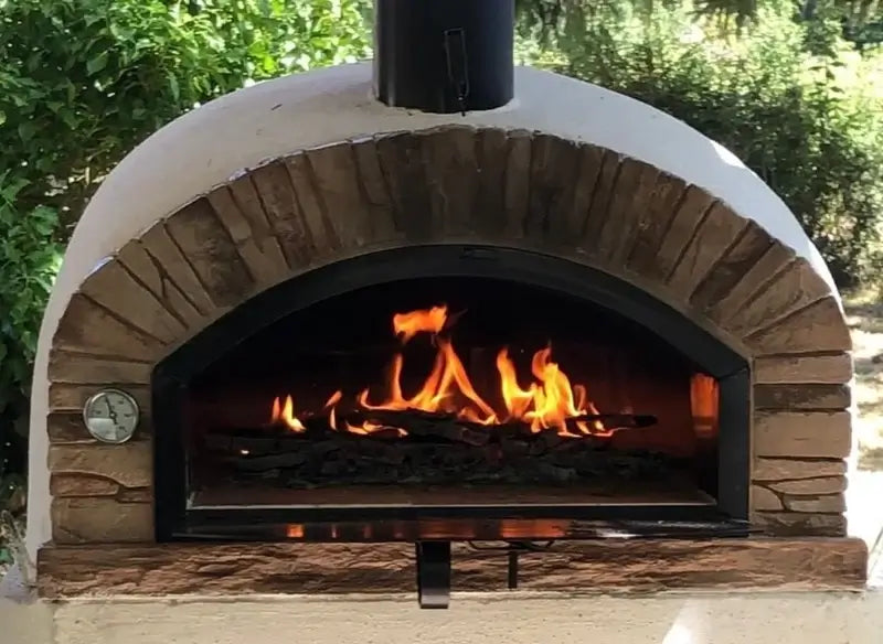 Buena Ventura Sierra brick pizza oven with a full fire burning and the door lowered under a covered patio