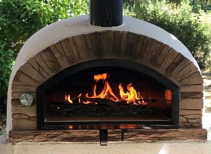 Buena Ventura Sierra brick pizza oven with a full fire burning and the door lowered under a covered patio