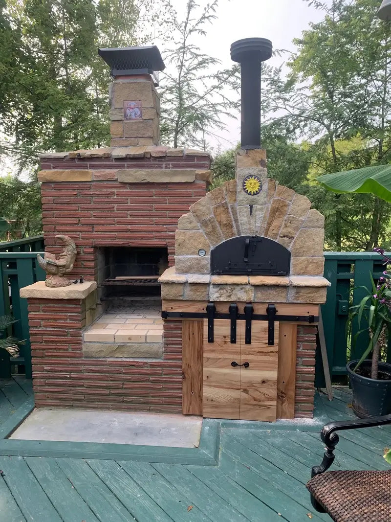 Builders custom Pizzaioli dome clad by its owner in brick and cut stone with a sun tile, a brick chimney, a black iron door, and a wood store below, on a deck