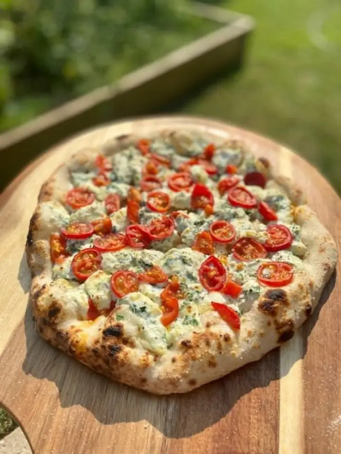Wood fired white pizza with cherry tomatoes and herbs on a wooden board outdoors