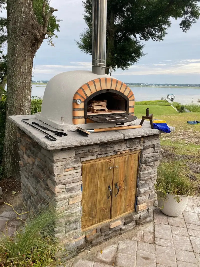 Pizzaioli Premium set on a stacked stone base in a waterfront outdoor kitchen with tools laid out