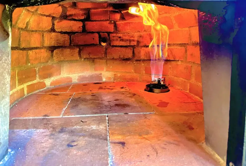 Gas burner head on the cooking floor of an Authentic Pizza Ovens brick oven with the pre drilled port in the rear wall