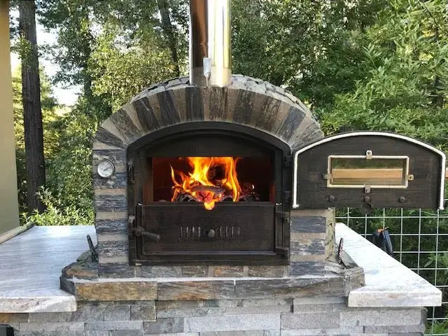 Lisboa Stone Finish pizza oven built into a stone outdoor kitchen counter with the Dutch door open and a fire burning