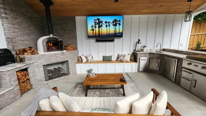Lume Alto Premium pizza oven lit in the corner of a covered outdoor living room with a fireplace, seating, and kitchen