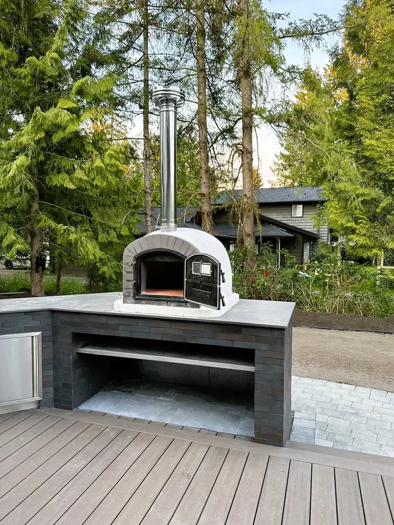 Lume Alto Premium pizza oven on a dark tile outdoor kitchen base beside a deck with the stainless chimney extension and cap fitted