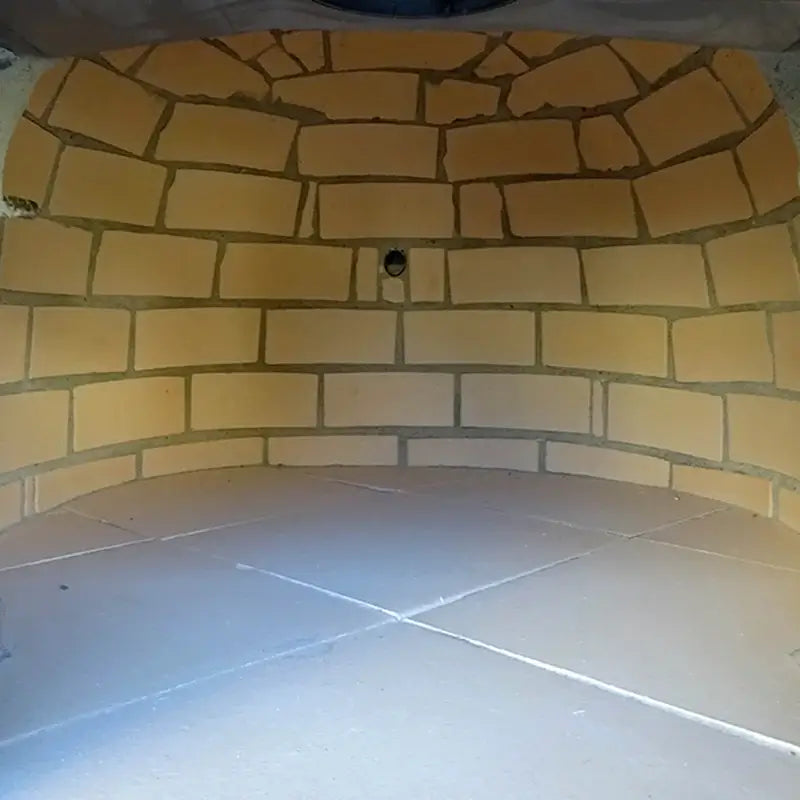 Inside the Lume Alto Tudo pizza oven: fire brick dome, tiled cooking floor, and the rotisserie spit hole in the rear wall