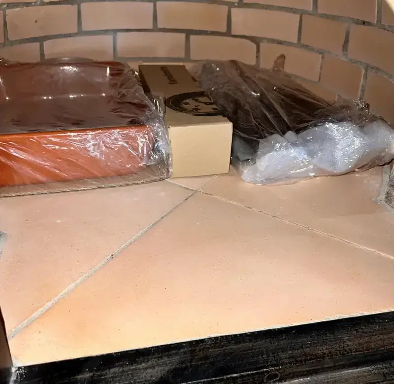 The included ceramic baking dish, thermometer box, and Ultra Fire kit packed on the floor of a Lume Largo pizza oven as delivered