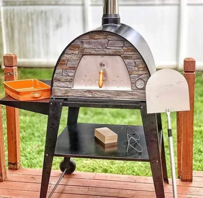 Black Maximus Mobile pizza oven on the Authentic Pizza Ovens stand on a deck with the included stainless peel and orange ceramic baking dish beside it