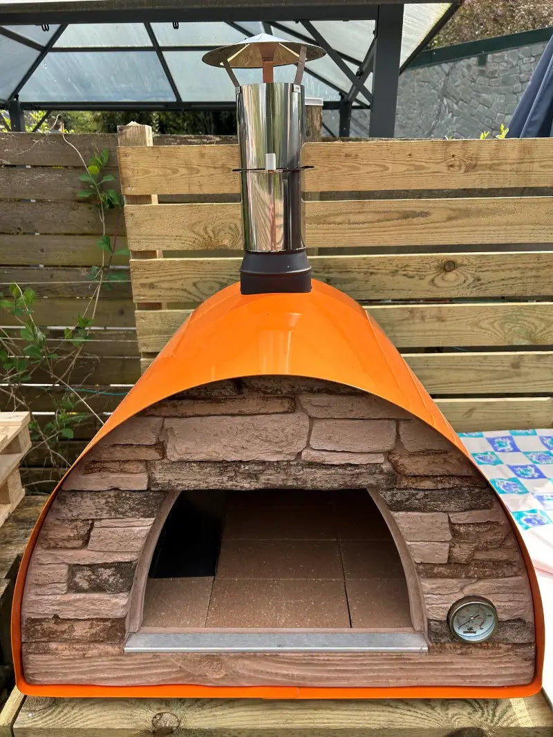 Orange Maximus Mobile pizza oven with the door removed, showing the arched mouth and the refractory tile cooking floor