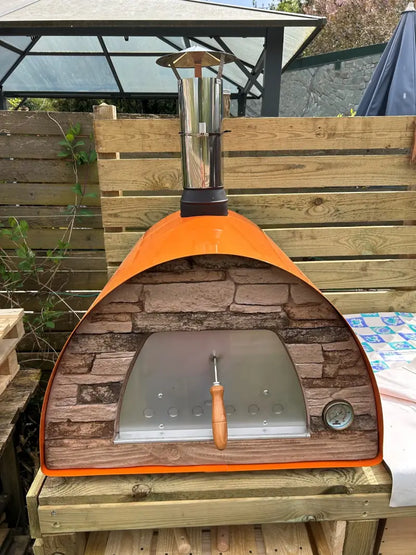 Maximus Mobile pizza oven in Orange straight on, sand toned stacked stone front around the stainless door with air holes and the dial thermometer at the right