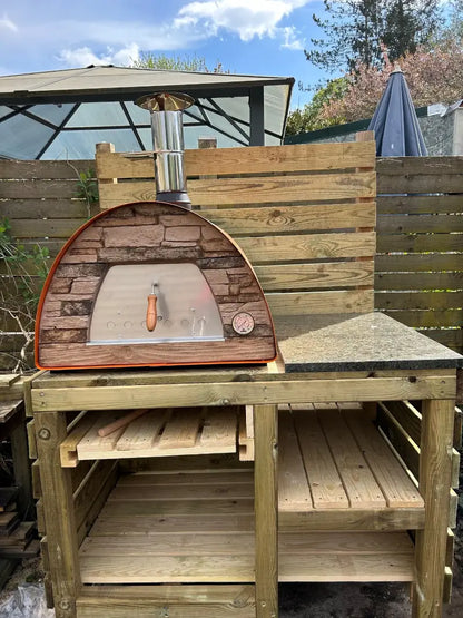 Orange Maximus Mobile pizza oven on a homemade timber bench with a granite landing beside it under a garden gazebo
