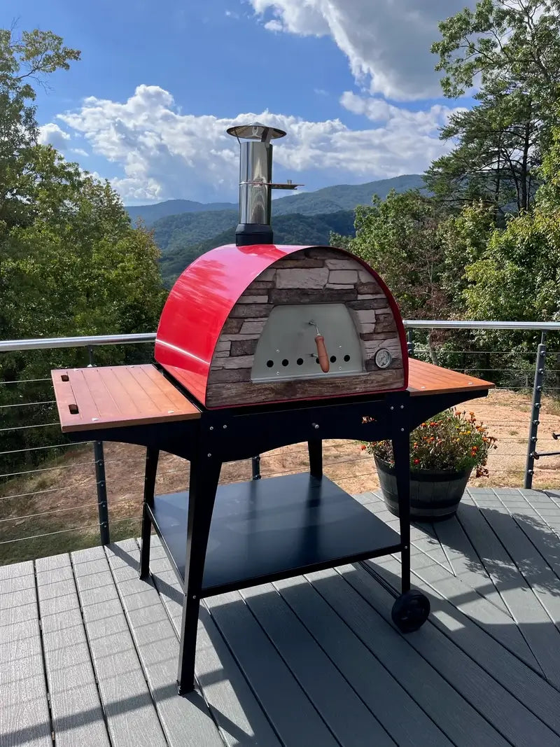 Red Maximus Mobile pizza oven on the Authentic Pizza Ovens stand with wooden side shelves on a deck overlooking wooded mountains