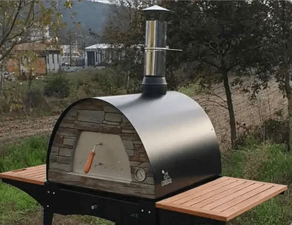 Black Maximus Mobile pizza oven sitting on the Woody stand with the wood slat shelves out on both sides, seen from the front corner