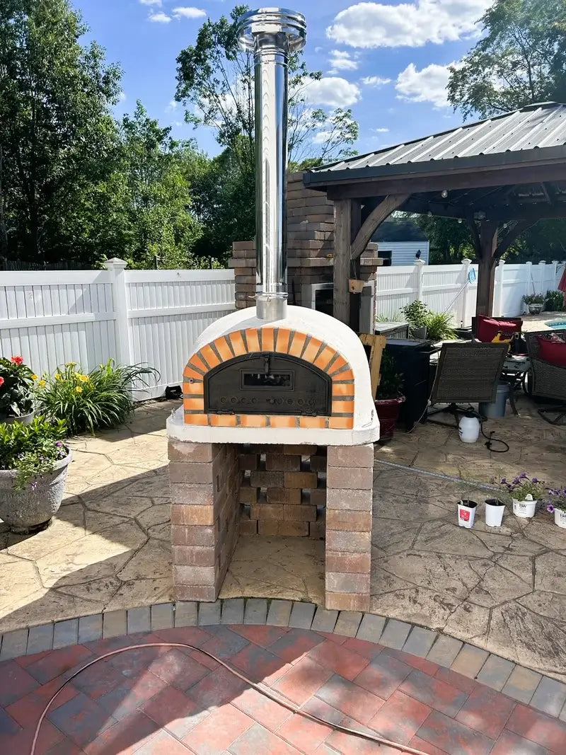 Pizzaioli Premium installed on a brick base on a patio with the stainless chimney extension and rain cap fitted