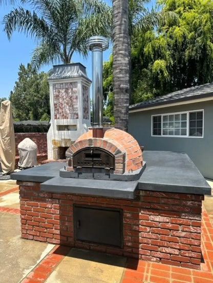 Rustic Pizzaioli installed on a red brick base with a poured concrete counter and stainless chimney extension in a California backyard