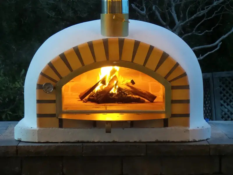 Pizzaioli Standard brick pizza oven at dusk with a full fire lighting the terracotta arch and white dome
