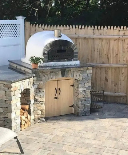 Pizzaioli Stone Arch installed on a fieldstone base with wooden storage doors and a granite counter on a paver patio