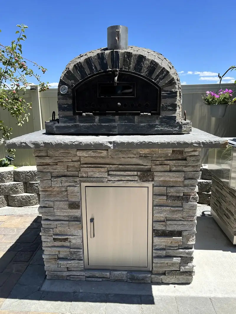 Pizzaioli Stone Finish installed on a stacked stone base with a bluestone counter and stainless access door on a paver patio