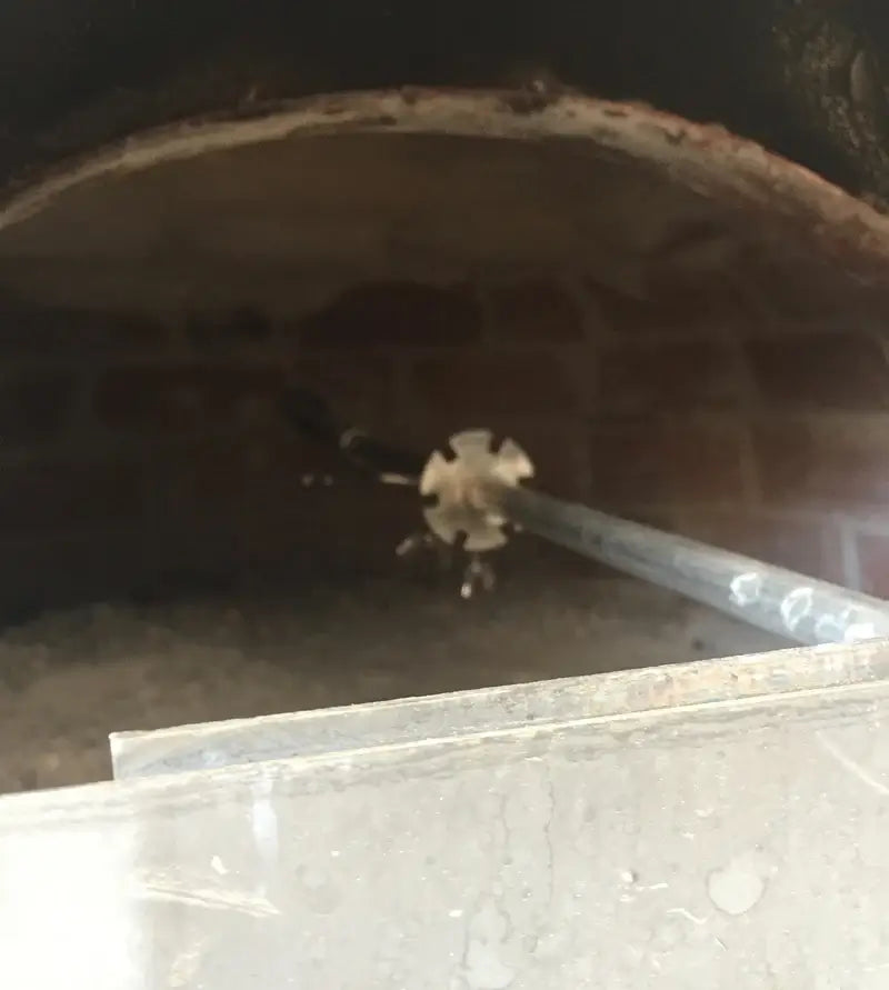 End of the Authentic Pizza Ovens rotisserie spit seated in the metal cap insert at the back of the brick oven dome