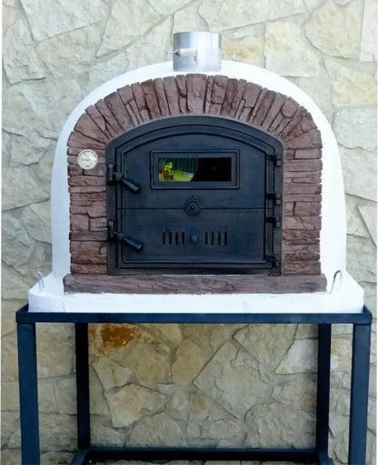 Ventura Sierra pizza oven with reddish brown stacked stone facade on a black steel stand against a natural stone wall, dial thermometer fitted