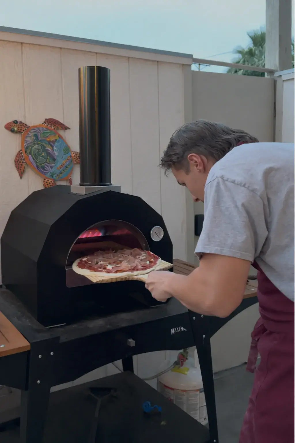 Pizza going into the ItaliaForno Bambino on a stand with the propane tank on the shelf below