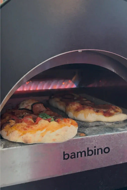 Two small pizzas cooking side by side on the ItaliaForno Bambino floor with the rear burner lit